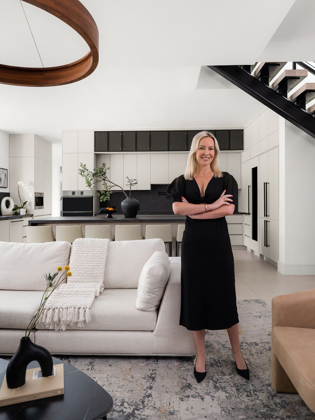 Interior designer Laure Nell stands confidently in a modern Boca Raton kitchen with sleek cabinetry, neutral tones, and a sculptural staircase, showcasing her refined, contemporary design style.