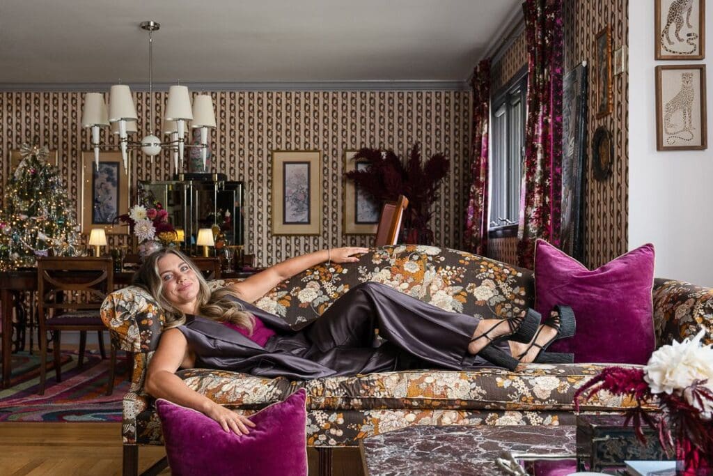 A maximalist holiday setting unfolds—featuring multiple tinsel-draped Christmas trees, a formal dining area, and patterned wallpaper that evokes retro glamour.