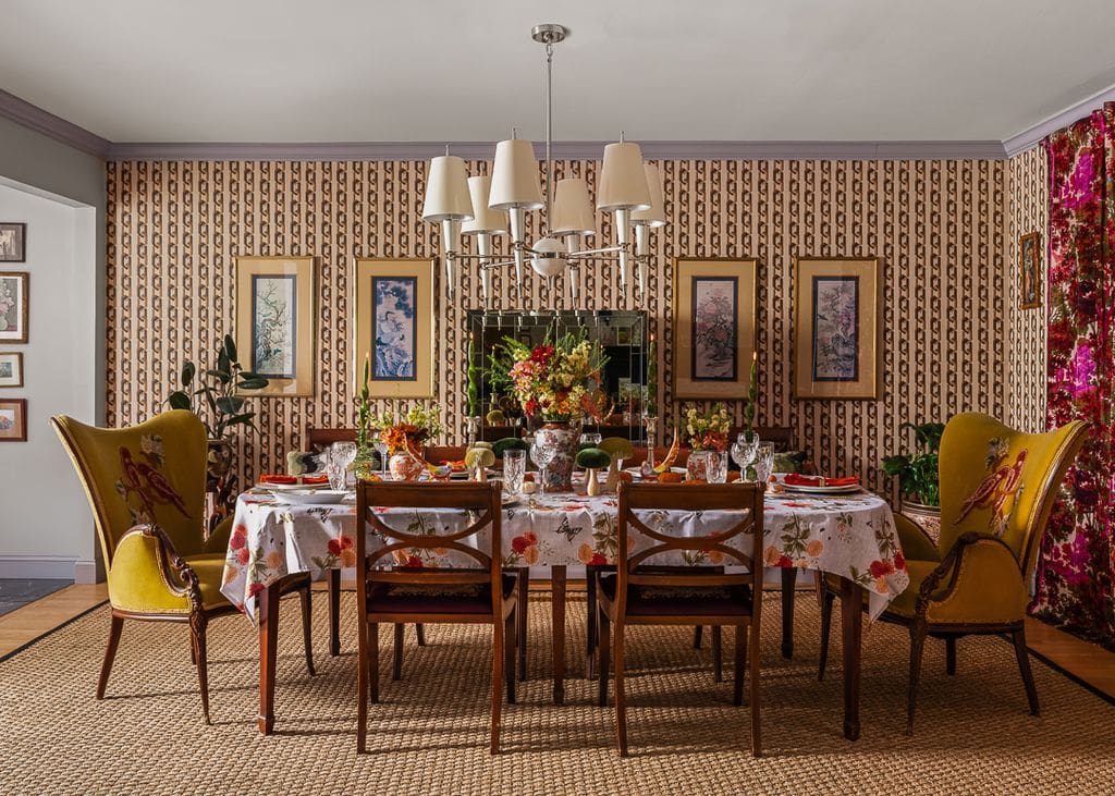 A richly layered fall dining room with vintage wallpaper, botanical wall art, and velvet wingback chairs, styled by interior designer Victoria Freise.Editorial interior photography captures this maximalist dining space, blending nostalgic charm with curated color and texture for a holiday-ready, designer home.