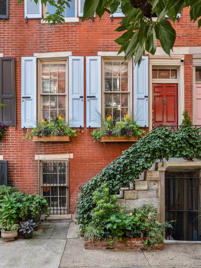 Front elevation of a Philadelphia townhouse with ivy cascading down the stair railing and layered greenery in planters below, designed and styled by Flornamentum. A sophisticated mix of organic form and architectural balance.