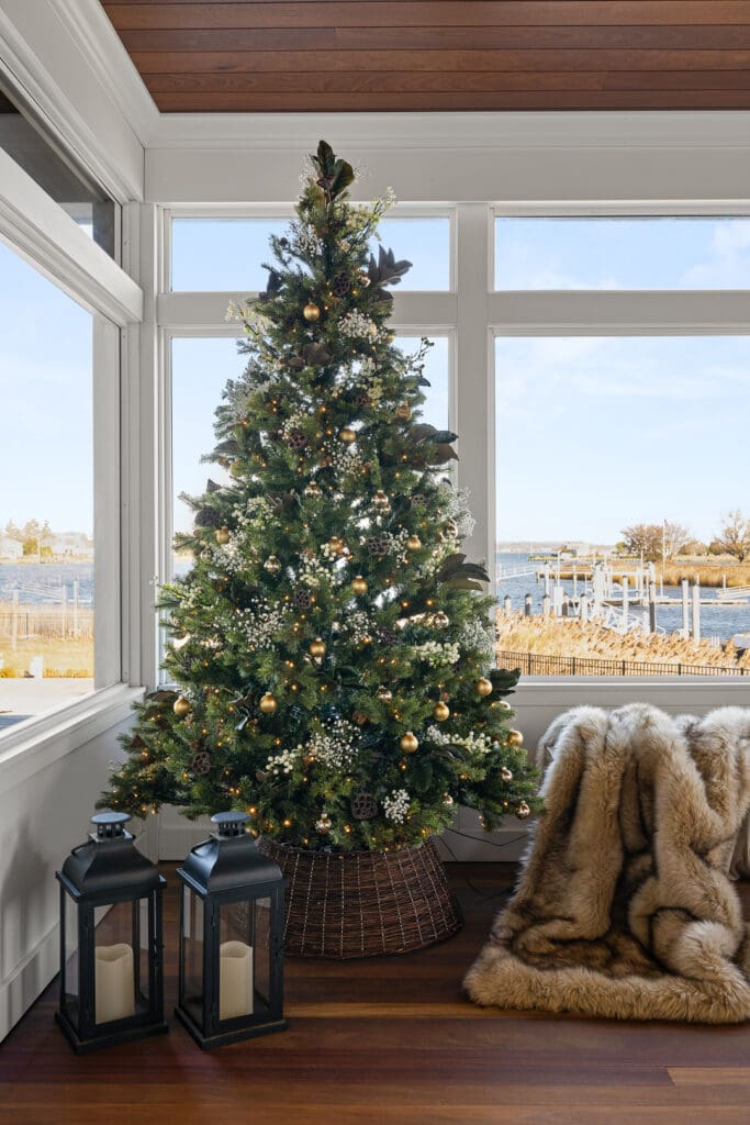 Christmas tree in a coastal farmhouse living area designed by Ginny Padula, decorated with soft whites and botanicals, photographed by Tori Sikkema with natural light emphasizing the serene waterfront view.